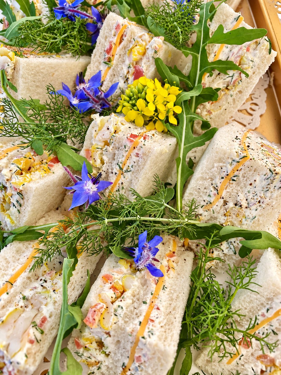 Plateau de petits sandwichs au pain de mie garnis de crème, décorés de fleurs de bourrache bleues, de fleurs jaunes, d'aneth et de roquette.